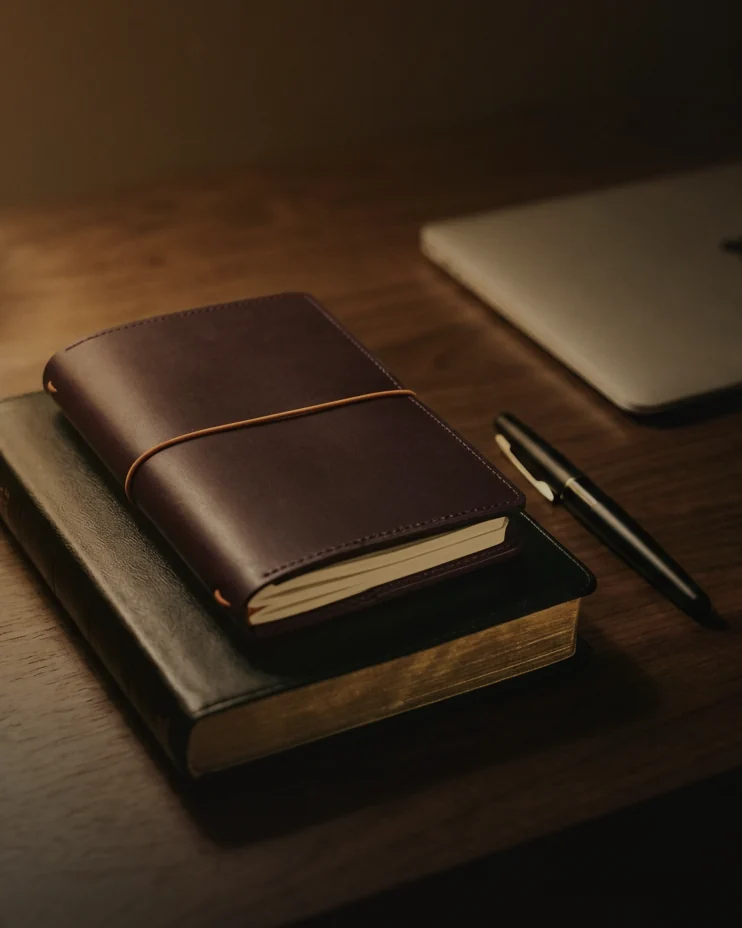 A Bible, a leather traveler's journal and a pen on a desk at night